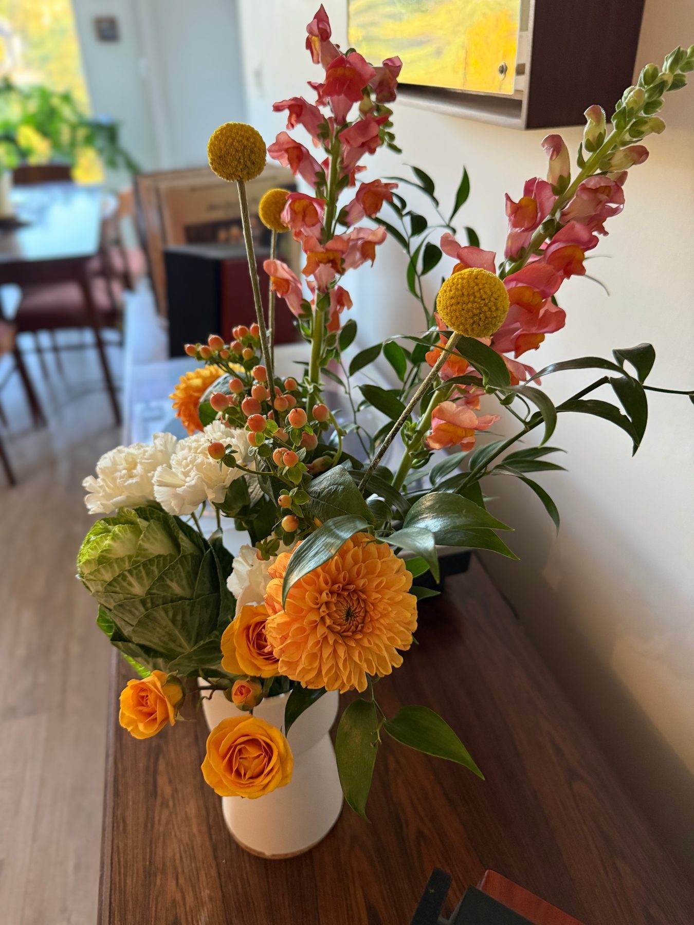 Orange dahlia, snapdragon and rose arrangement with cabbage foliage, styled on a wooden table