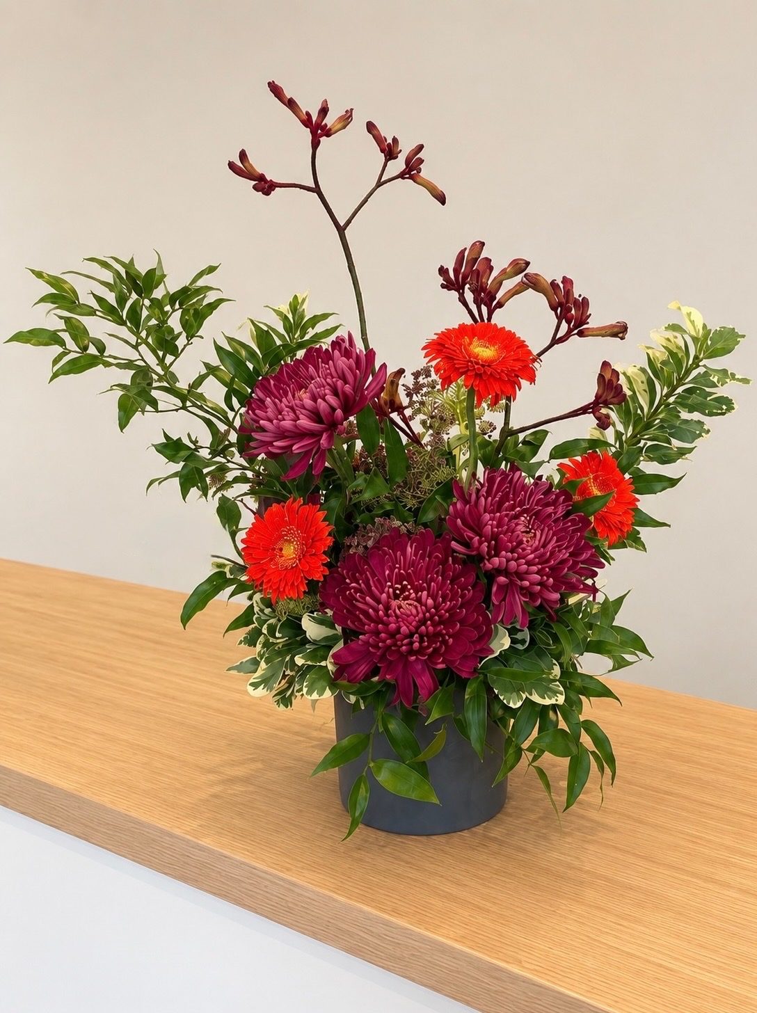 Deep red chrysanthemum and orange gerbera daisy arrangement in a dark vase