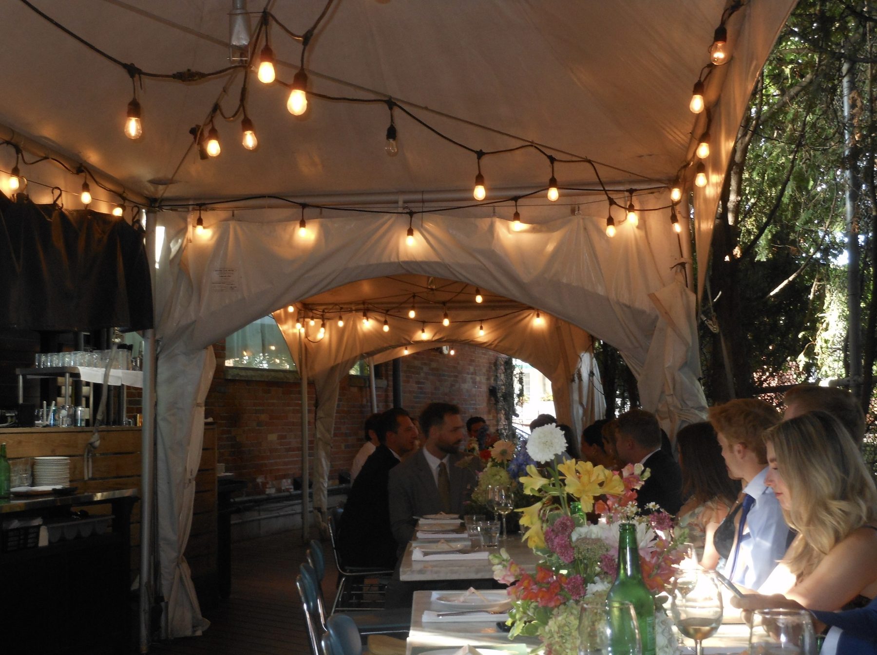 Outdoor tented dinner with floral centerpieces and string lights