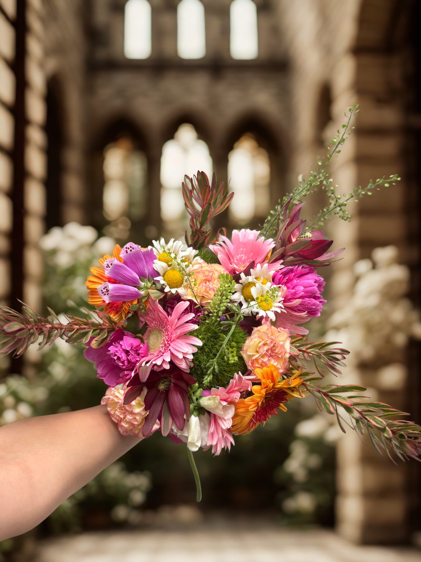 Vivid pink, purple and orange hand-tied bouquet held up in front of a stone cathedral